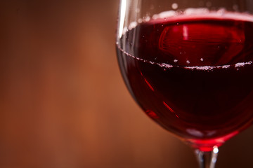 Elegant and fragile wineglass of tasty red wine against brown wooden background close-up.