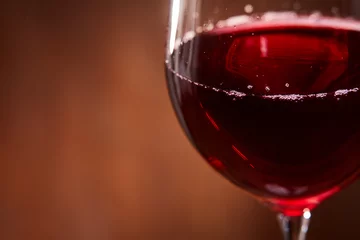Fotobehang Elegant and fragile wineglass of tasty red wine against brown wooden background close-up. © Aleksey