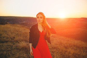 Happy woman enjoying nature sunset dressed in a red long dress and a black leather jacket