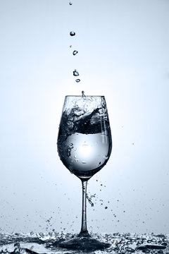 Bubbles of drinking water falling in the wineglass standing on the glass with droplets against light background.