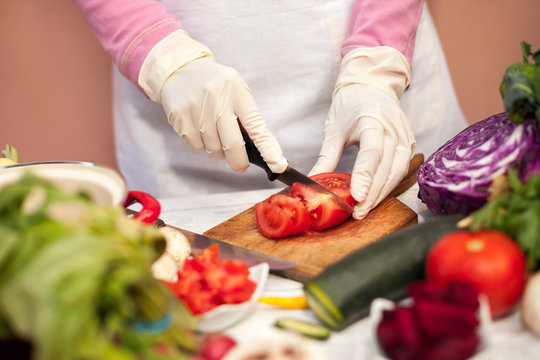 Female with gloves slicing tomato
