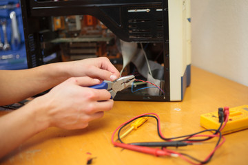 Young man hands cutting a wire of computer and trying to repair (color toned image)