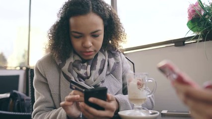 Closeup of Attrcative mixed race woman using credit card shopping online with smartphone in street cafe while have coffee break with her friend