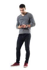 Stylish young trendy man typing message on cellphone. Full body length portrait isolated on white...