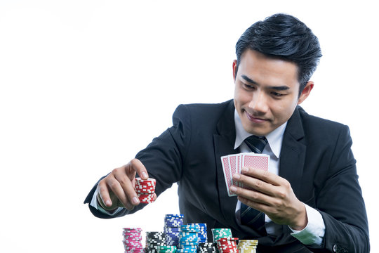 Portrait young man in black suit is putting stack of chips and holding poker card