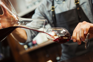 Sommelier pouring wine into glass from mixing bowl. Male waiter