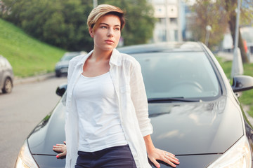 Portrait of stylish young pensive woman leaning on car