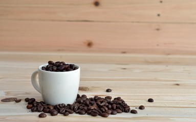 coffee beans from the white ceramic cup on wooden background