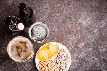 Beer in bottles and glasses closeup on the concrete table. Beer and snacks are pistachio nuts, chips and nachos top view. Copy space. Drink and snack for the football match or party