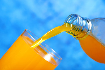 Orange juice pouring in a glass over blue background like a concept for summer drink 