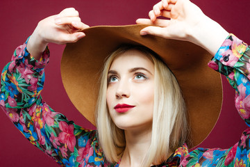 Beautiful Blonde Model Wearing Fashionable Hat and Colorful Shirt is Posing on Pink Background in Studio.