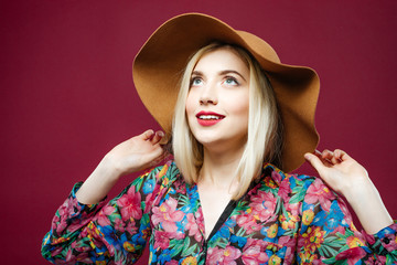 Smiling Woman in Colorful Shirt and Hat is Posing on Pink Background. Amazing Blonde Model with Long Hair in Studio.