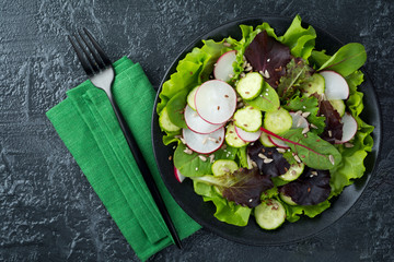 Salad with fresh radishes, arugula, beets, chard, sunflower seeds, flax and sesame seeds on a black background. Selective focus. top view. Copy space.