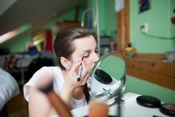 Fototapeta premium Young woman doing herself make-up, doing properly, looking concentrated
