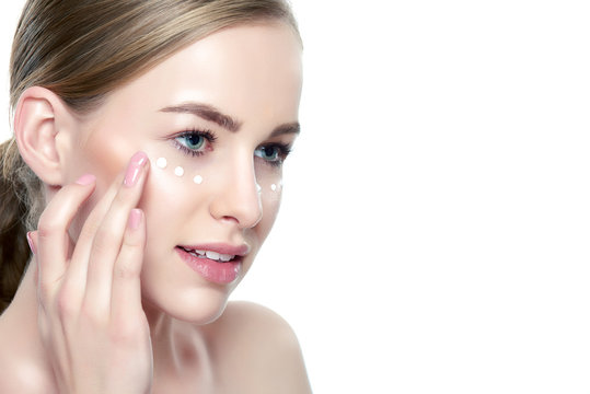 Beautiful Young Blond Woman applying Face cream under her eyes. Facial treatment. Cosmetology, beauty and spa concept. Isolated on white background.