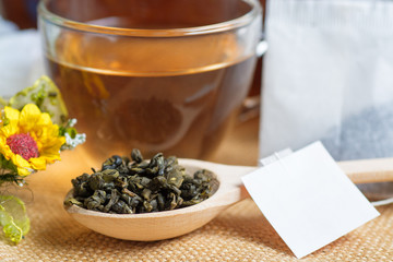 Tea in a glass cup with Dry (black and green) tea in wooden spoons, Herbal teabags on burlap tablecloths. 
