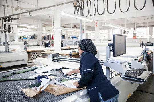 Factory worker removing cut textile pattern from pattern cutting machine in clothing factory