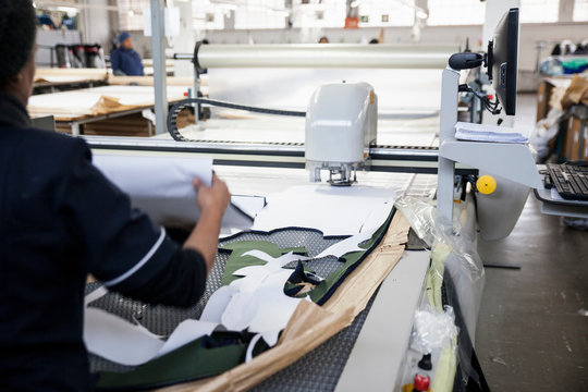 Rear view of factory worker removing cut textile pattern from pattern cutting machine in clothing factory