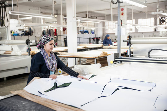 Factory worker removing cut textile pattern from pattern cutting machine in clothing factory