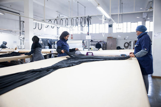 Factory workers unrolling textiles on work table in clothing factory