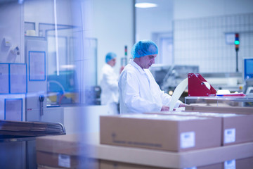 Workers packaging pharmaceutical products on production line in pharmaceutical plant