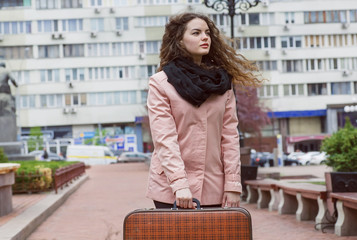 Fototapeta na wymiar Wind in hair of young woman with old style suitcase. She is traveling in a big city.