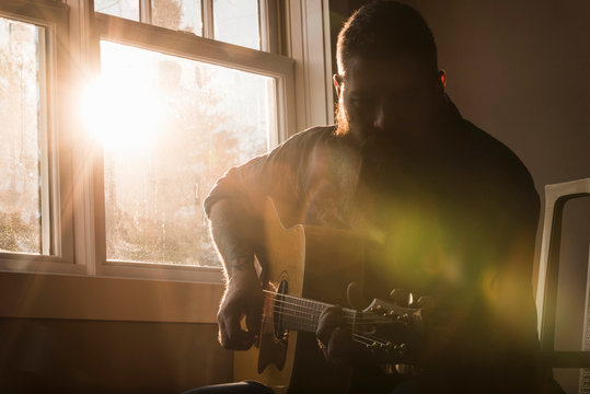 Man playing guitar beside window