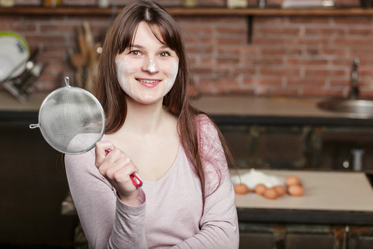 A woman stands in the kitchen on the background of a table with eggs and holds a sieve for sifting the flour