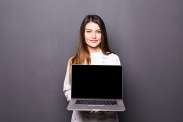 Smiling doctor woman pointing in laptops blank screen on grey