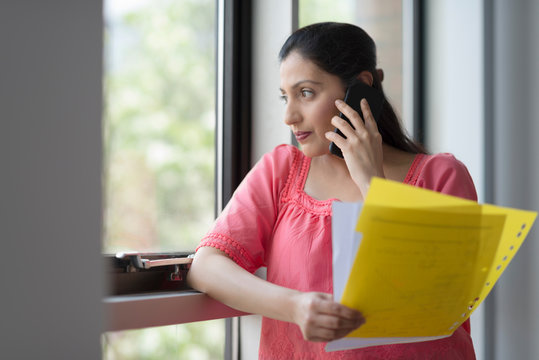 Woman holding papers on telephone call by office window