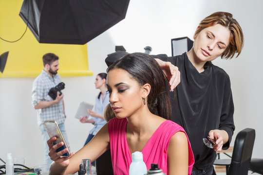 Hairdresser styling model's long hair in photography studio
