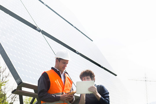 Male and female engineers looking at digital tablet on solar panel site