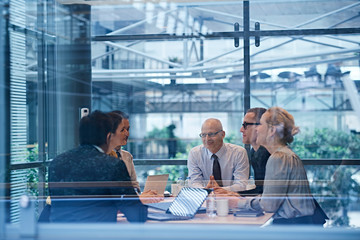 Window view of businesswomen and men having discussion in conference room