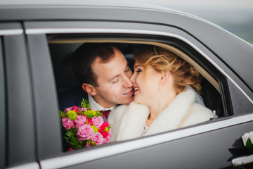 Loving newlywed bride and groom laugh in the retro wedding car