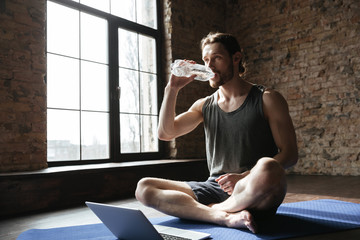 Sportsman in gym sitting on floor drinking water