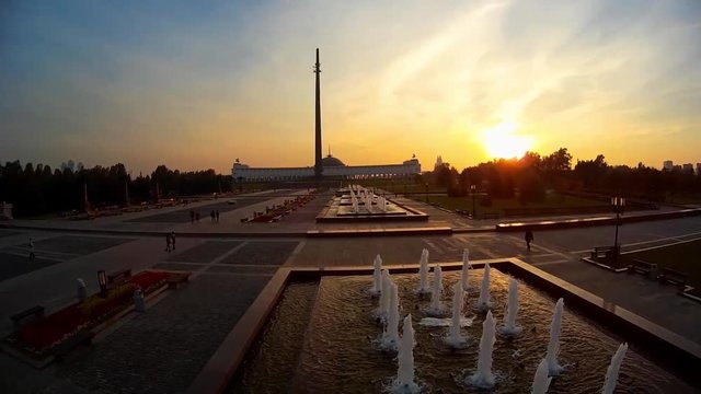 Poklonnaya Hill Victory Park Triumphal Arch statue of Nike monument of St George slaying dragon. Moscow Russia. People walk near fountains Best view. Summer orange sunset. Aerial Flight Close to above