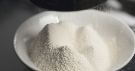 Handheld shot of sieving flour with mug sieve on plate closeup, 4k photo