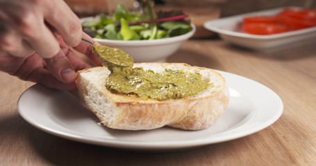 shot of pesto sauce put on ciabatta bread preparing sandwich, 4k photo