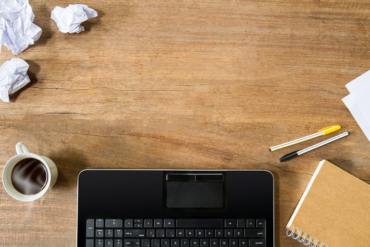 Computer laptop,coffee cup,notebook,crumpled paper and pens on vintage grunge wooden desk,daily business concept