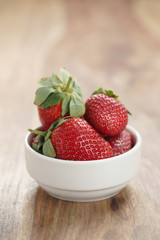 ripe organic strawberries in white bowl on wood table, with copy space