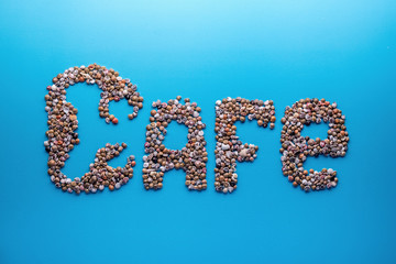 Inscription (word, sign) 'Cafe' made of seashells on blue paper background