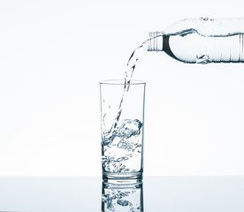 Pouring drinking water from bottle into drinking glass on white background