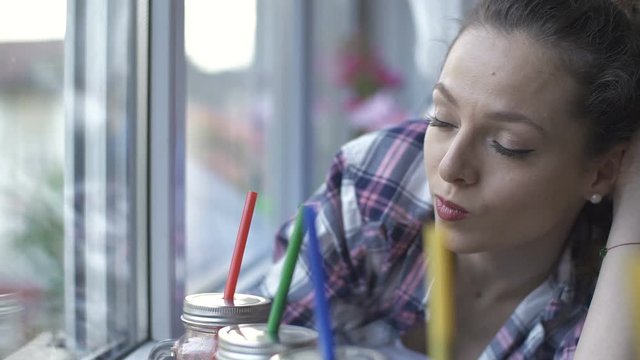 Close up of healthy woman drinking vegetable detox smoothie and looking by the window at home