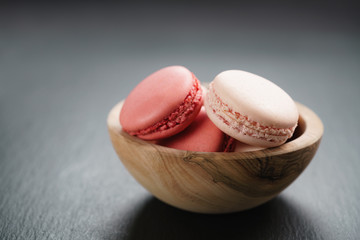 pink macarons in bowl on slate background with copy space, shallow focus