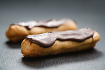 two eclairs with dark chocolate on top on slate background, shallow focus