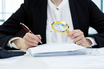 internal audit concept - woman with magnifying glass inspecting documents - obrazy, fototapety, plakaty