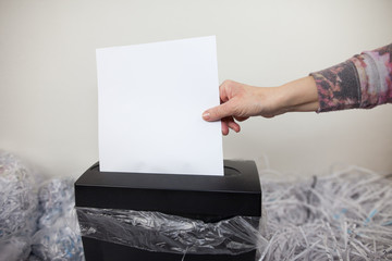 Senior woman hands shredding some white papers by automatic shredding machine