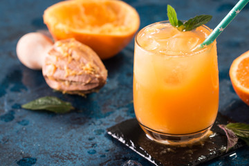 Orange juice in glass with mint, fresh fruits on dark blue background