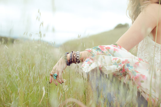 Cropped shot of boho woman wearing bangles and rings sitting in field of long grass