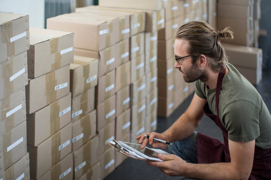 Man using digital tablet to check boxed products in factory storeroom